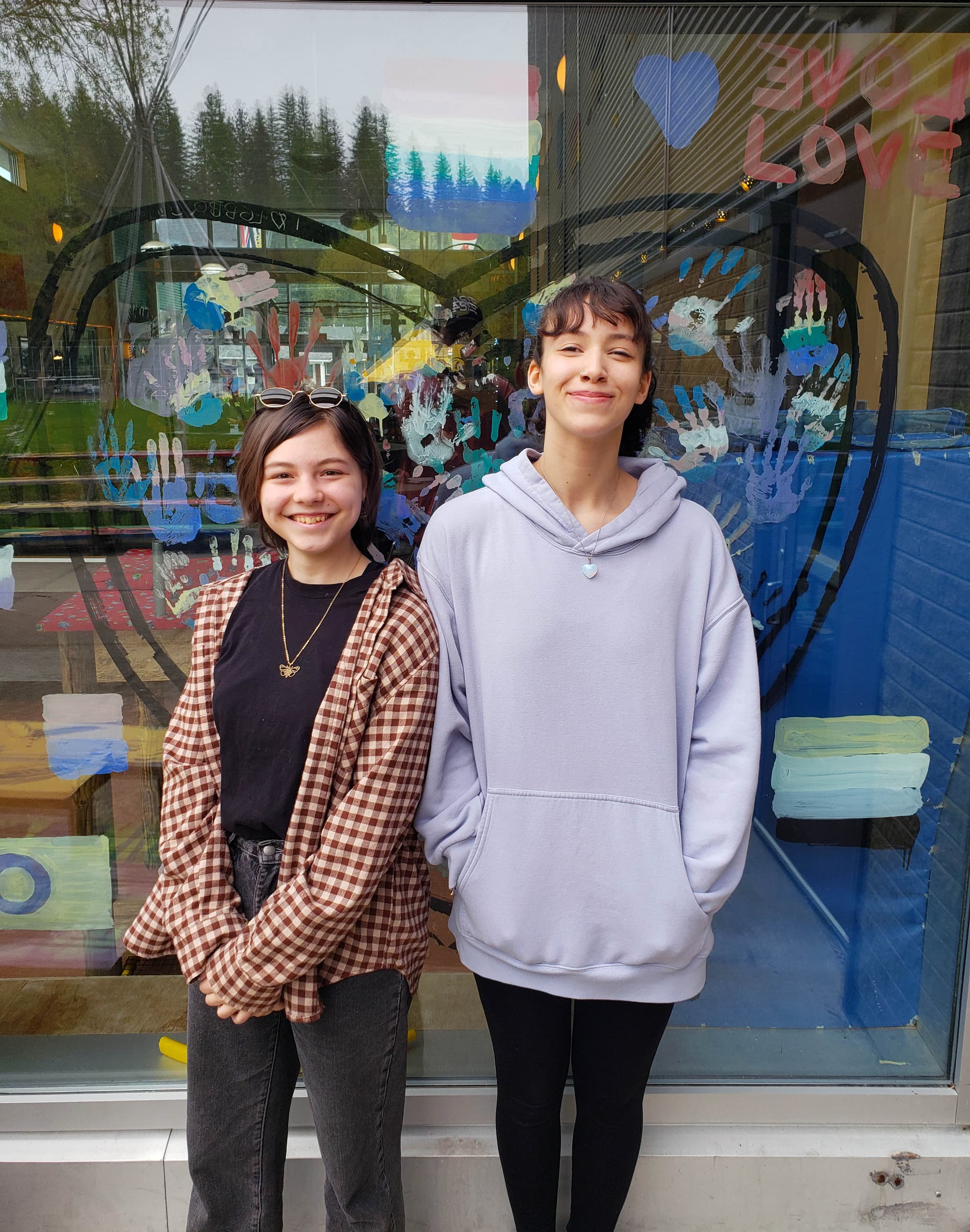 Two smiling female students standing in front of a shop window