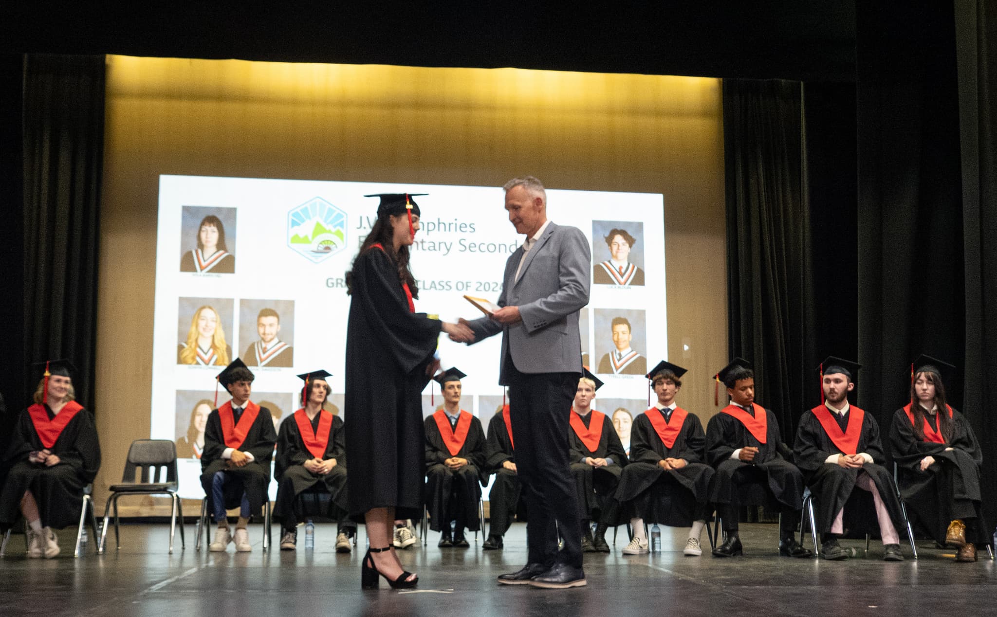 Young woman in cap and gown shakes hand of man in grey suit