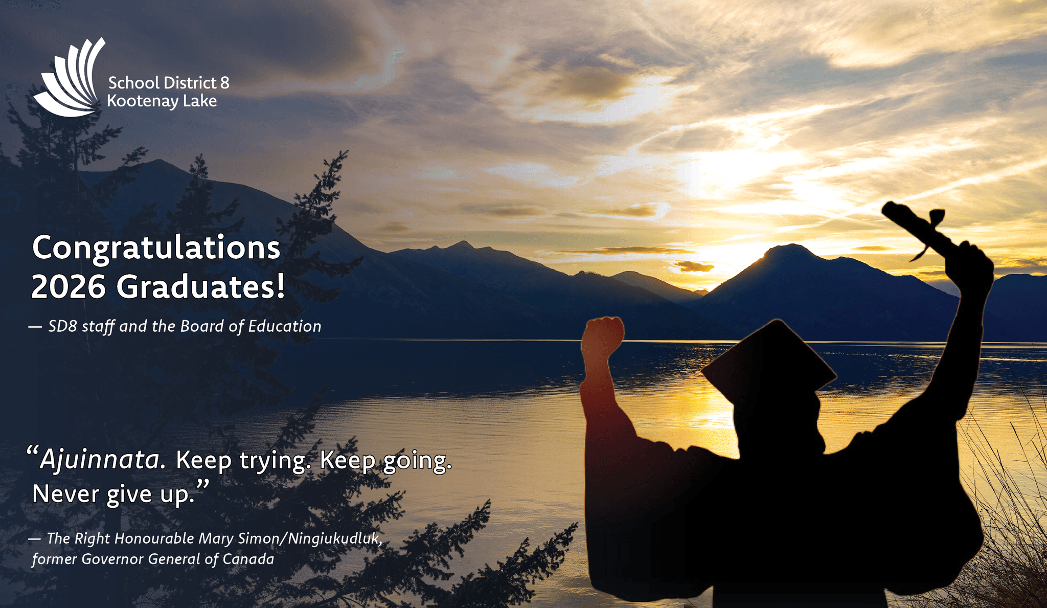 Silhouette of a person in cap and gown with arms raised holding a diploma, in front of a lake and mountains at sunset