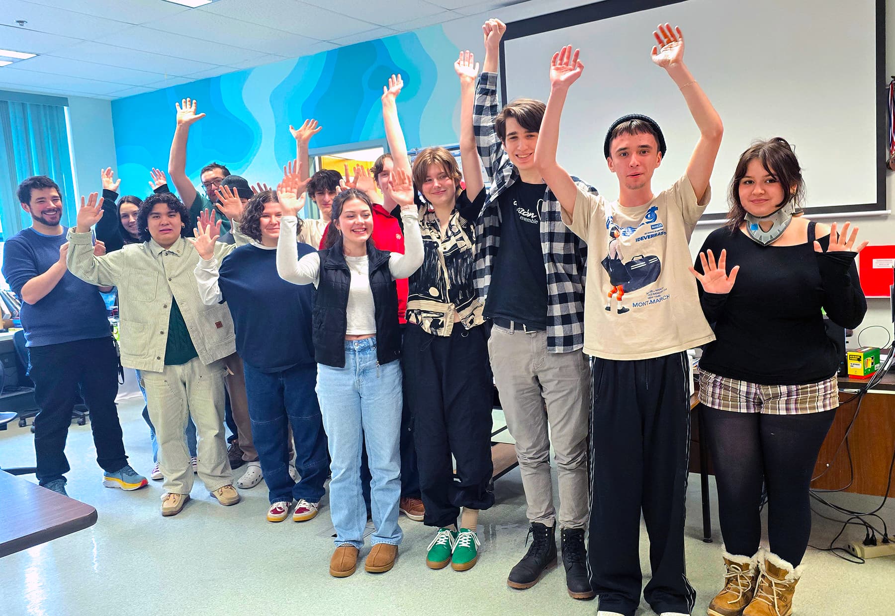 A group of young people and their teachers with hands raised in celebration in a school classroom