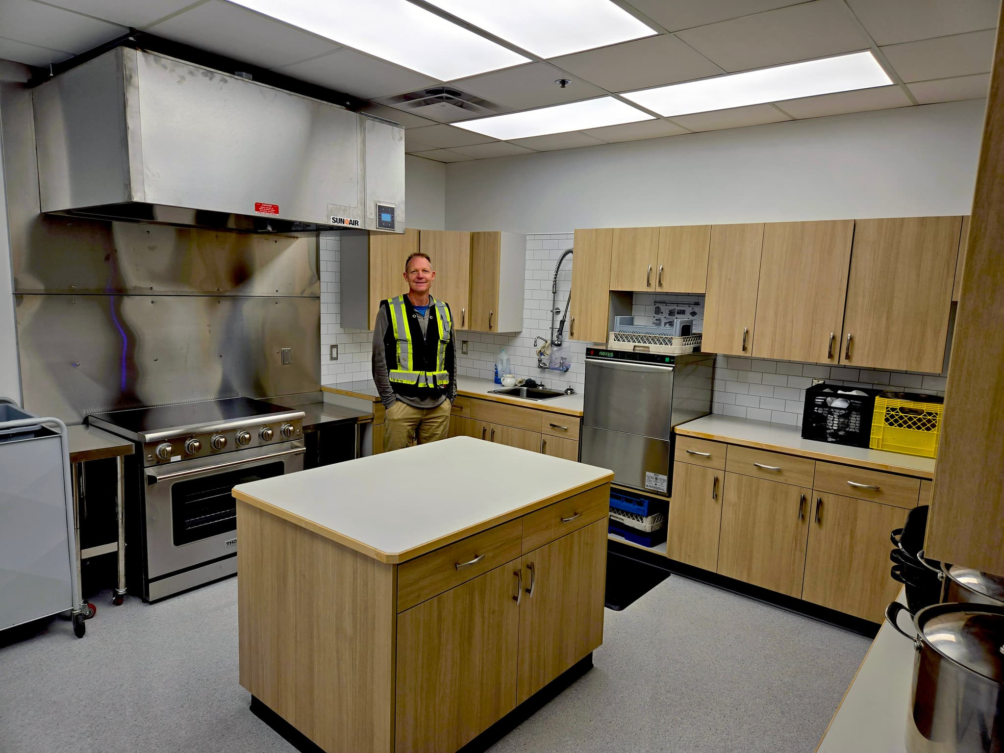 A carpenter wearing a reflective shirt stands in a newly renovated school kitchen.