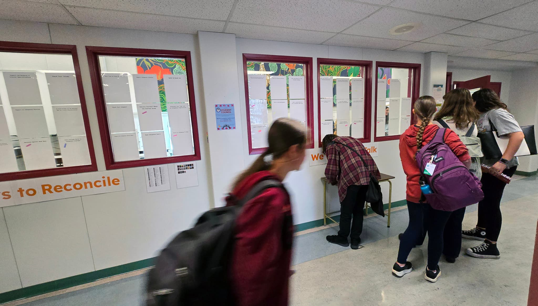 High school students gather at a table in front of a wall adorned with action post-its