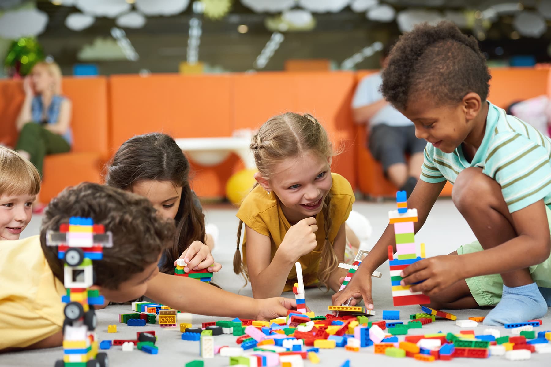 A group of young children play with lego on the floor in a play area.