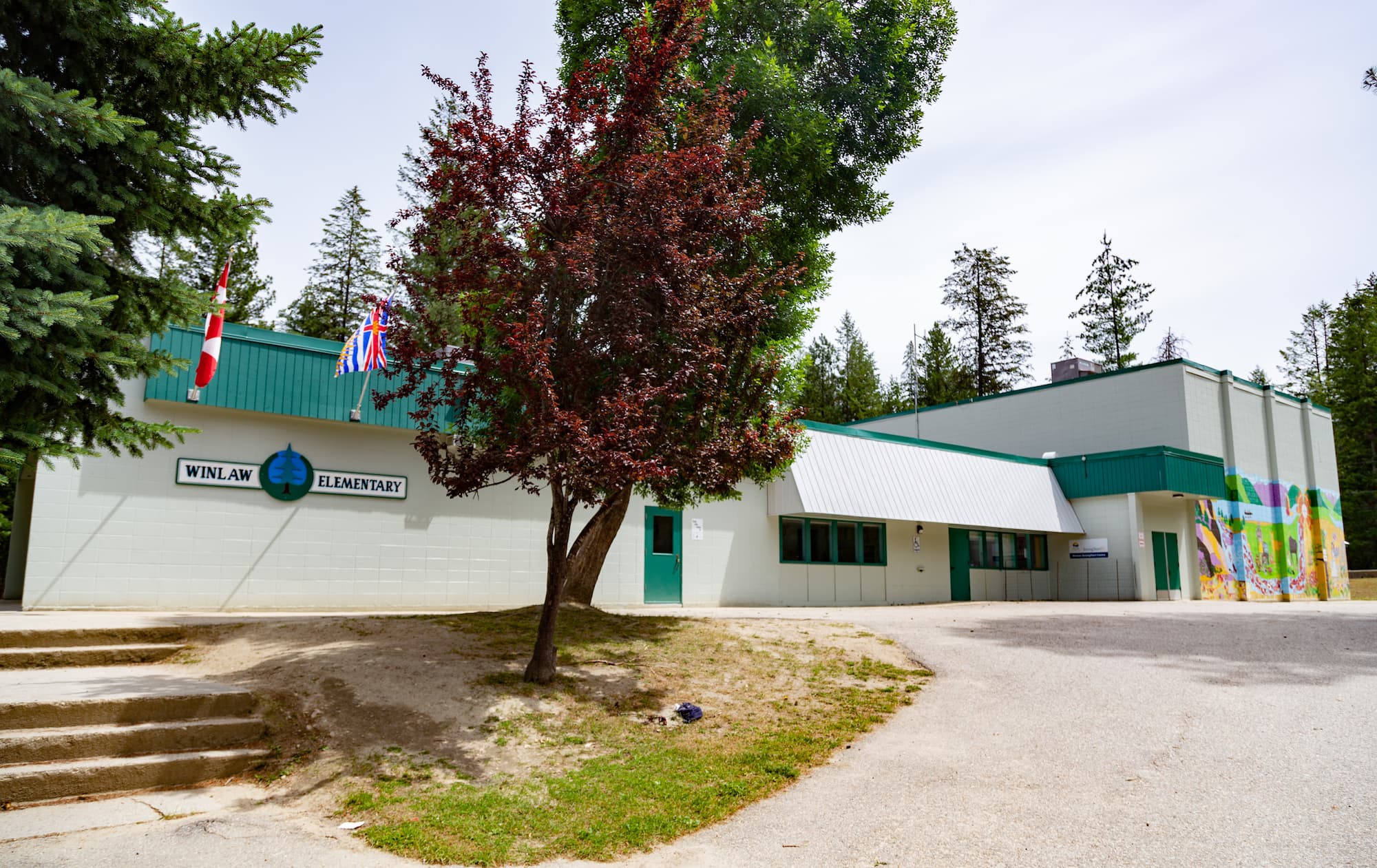 A white, stucco flat-roofed elementary school with green trim behind some trees
